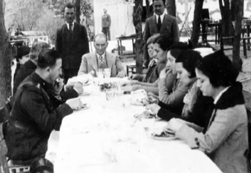 An outdoor table laid with a white cloth; a large group seated around it.